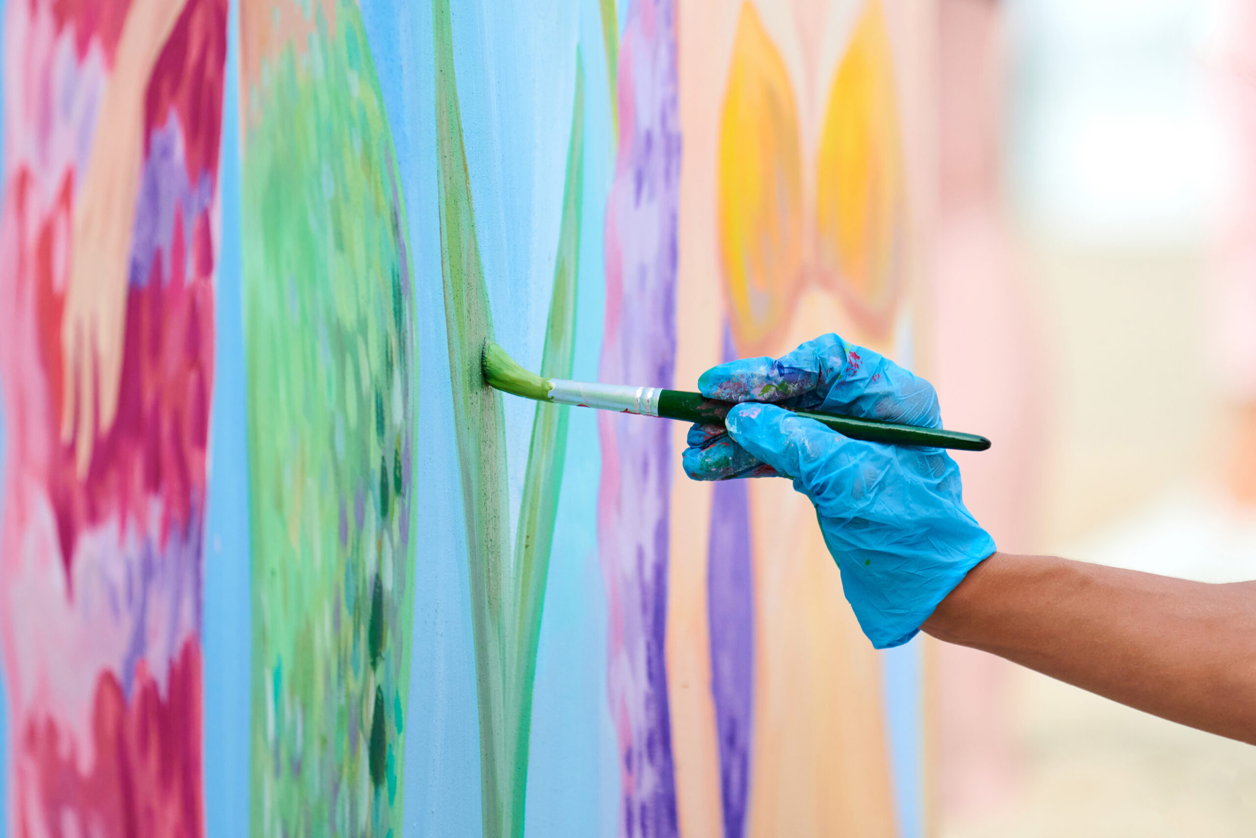 Artist's hand in blue gloves with paintbrush painting colorful picture at outdoor art festival