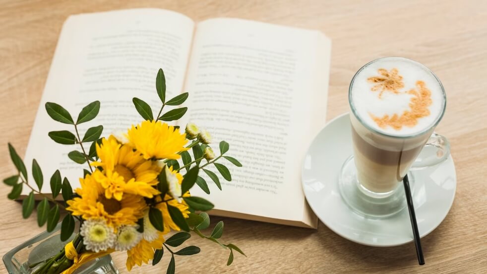 Ảnh bình hoa và ly cà phê latte với cuốn sách mở trên bề mặt kết cấu bằng gỗ